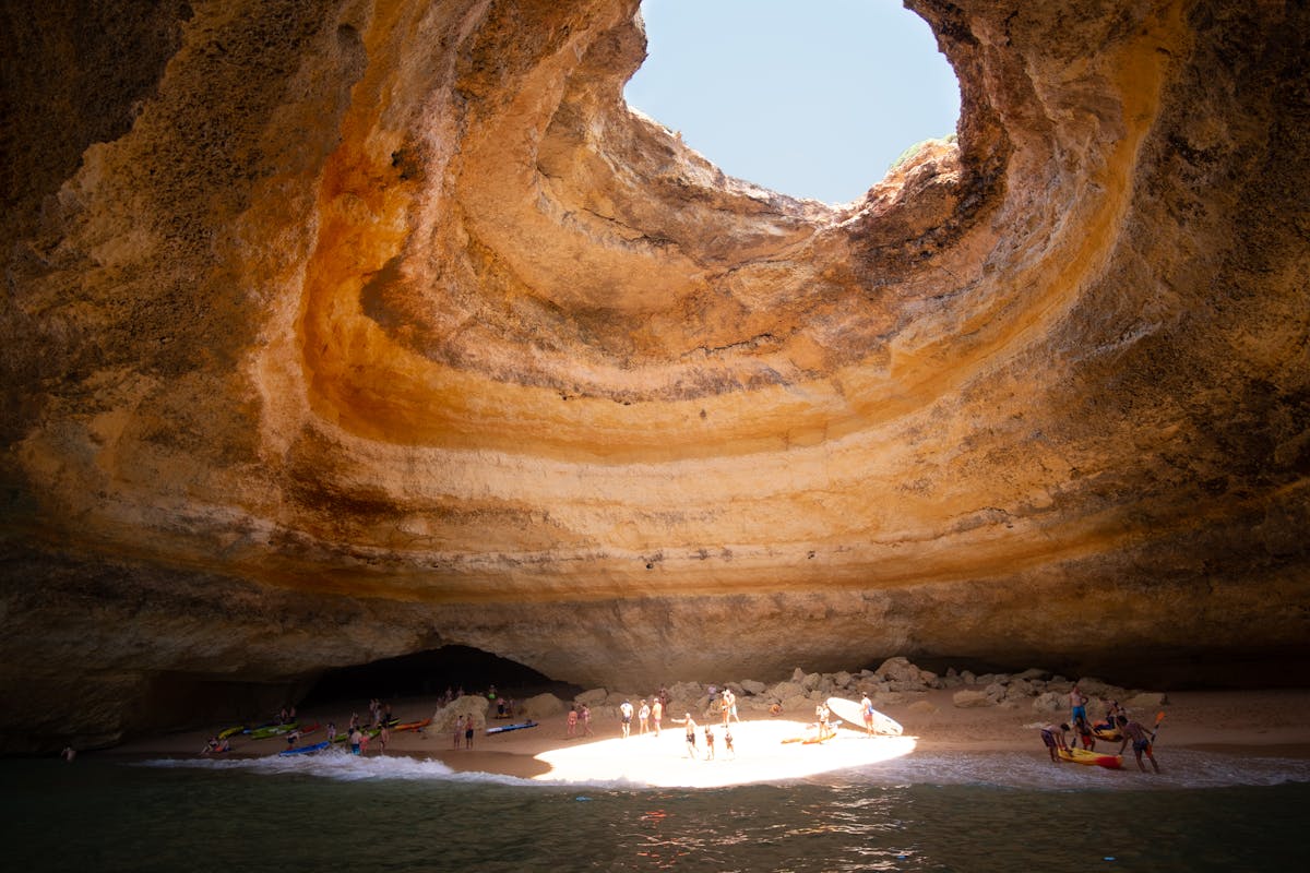Visitors inside the Benagil sea cave with sunlight through the roof opening in the Algarve