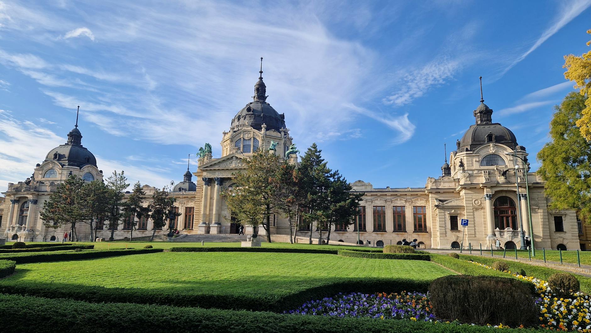 The neoclassical Széchenyi Thermal Bath building under a blue sky in Budapest.