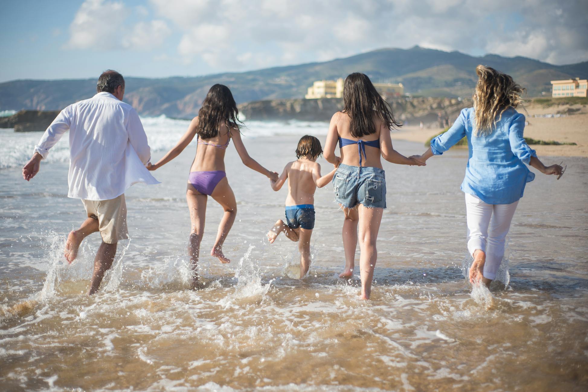 A family running joyfully into the ocean on a sunny beach on a UK bank holiday