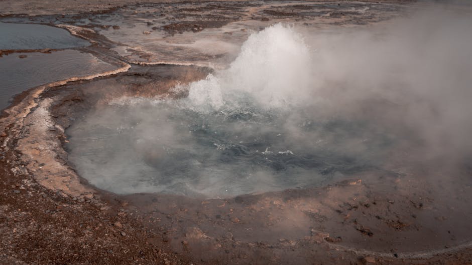 Geyser erupting a tall column of steam against a clear blue sky in Iceland