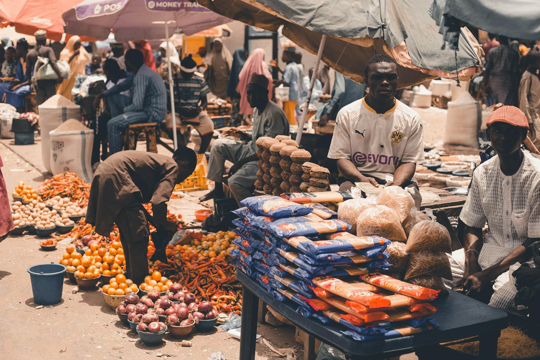 Vendors at a busy outdoor African market selling fresh produce under umbrellas