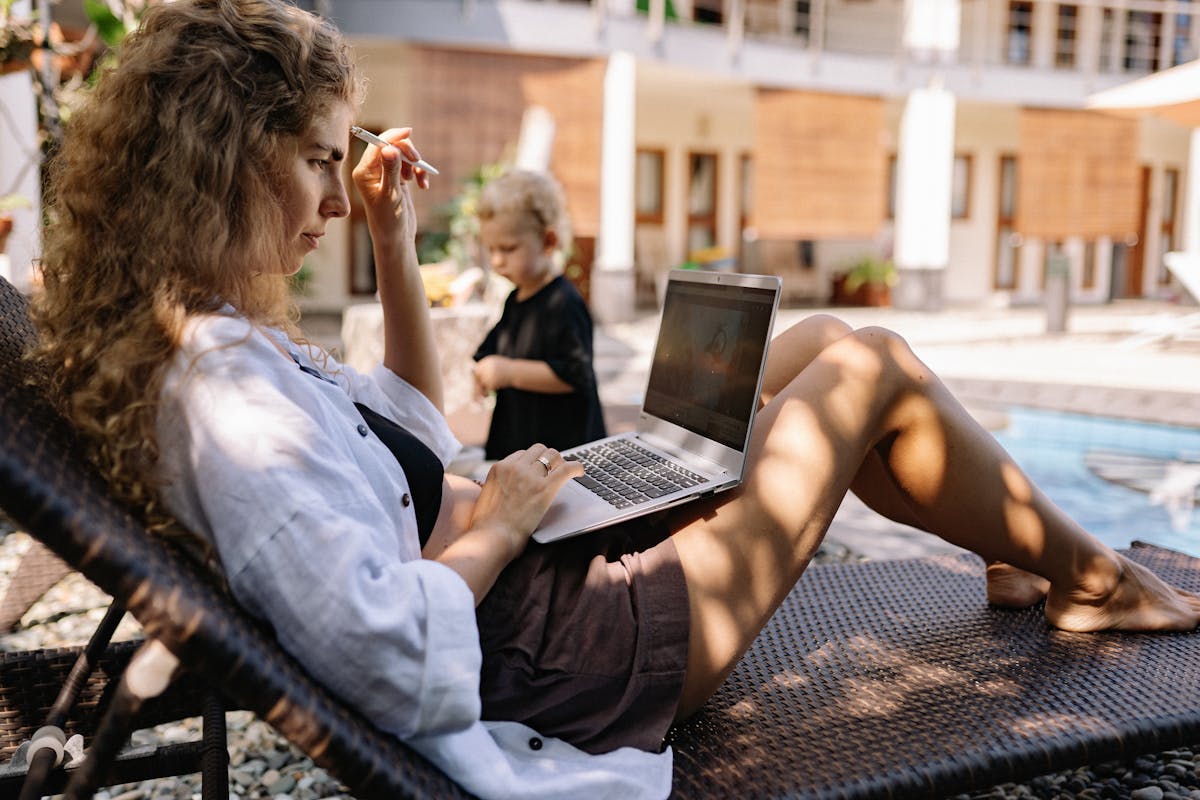 Woman relaxing on a sunlounger by a pool with a laptop, planning a holiday deal