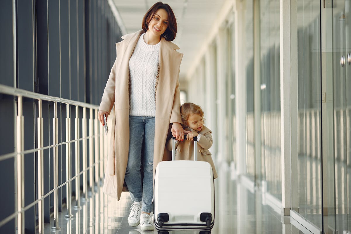 Mother and daughter smiling with a white suitcase in an airport corridor