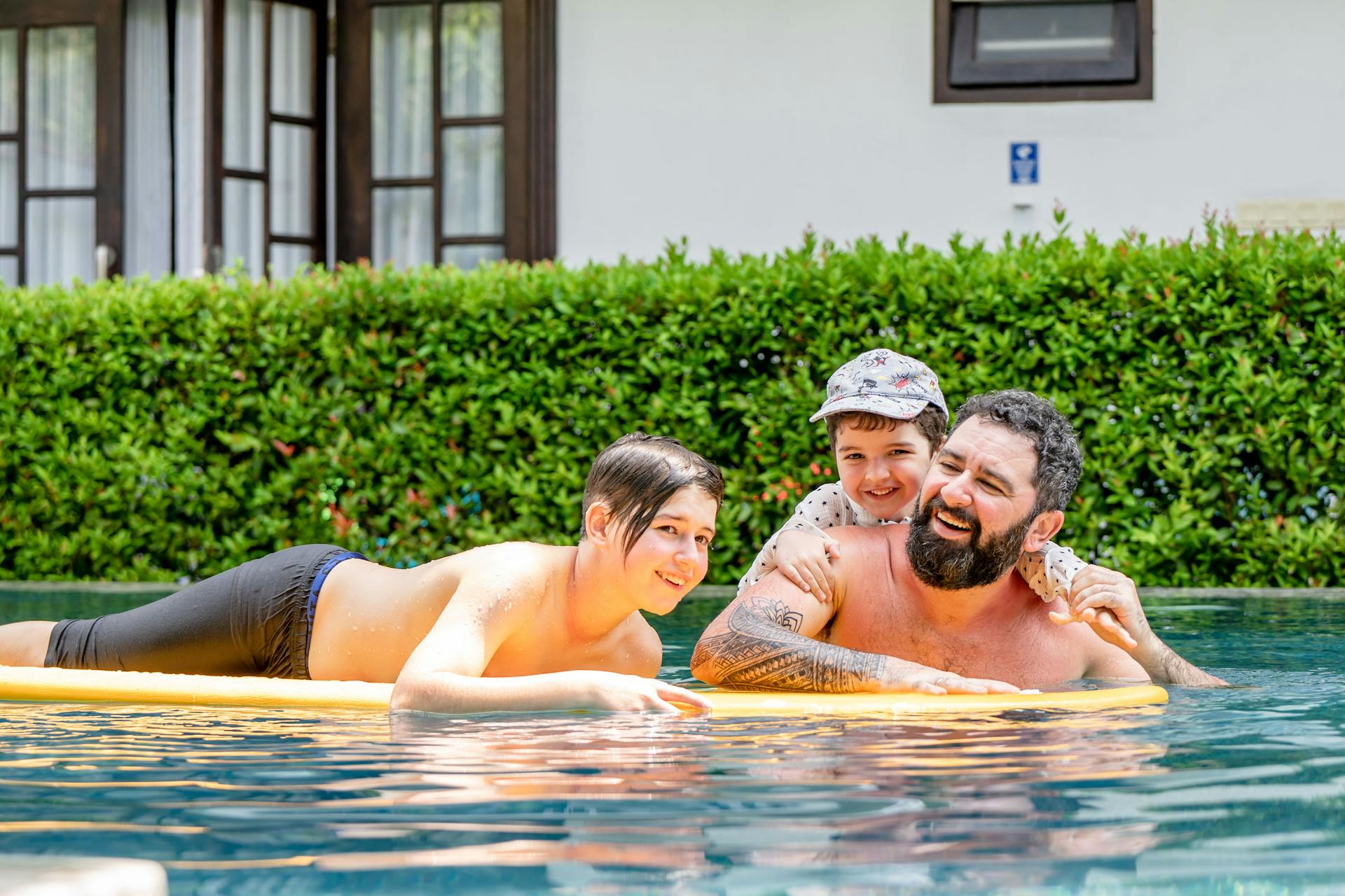 A father and children laughing on a pool float at a sunny holiday resort