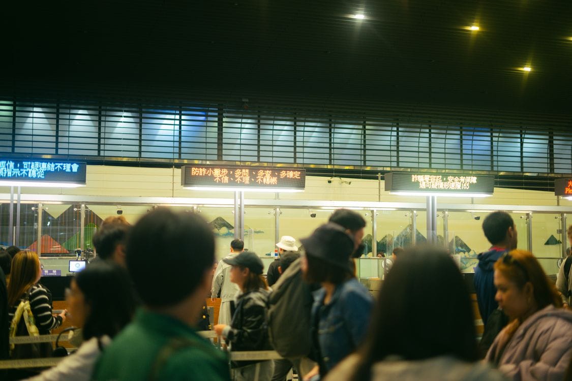 Crowded airport check-in area with passengers queuing and flight information screens visible