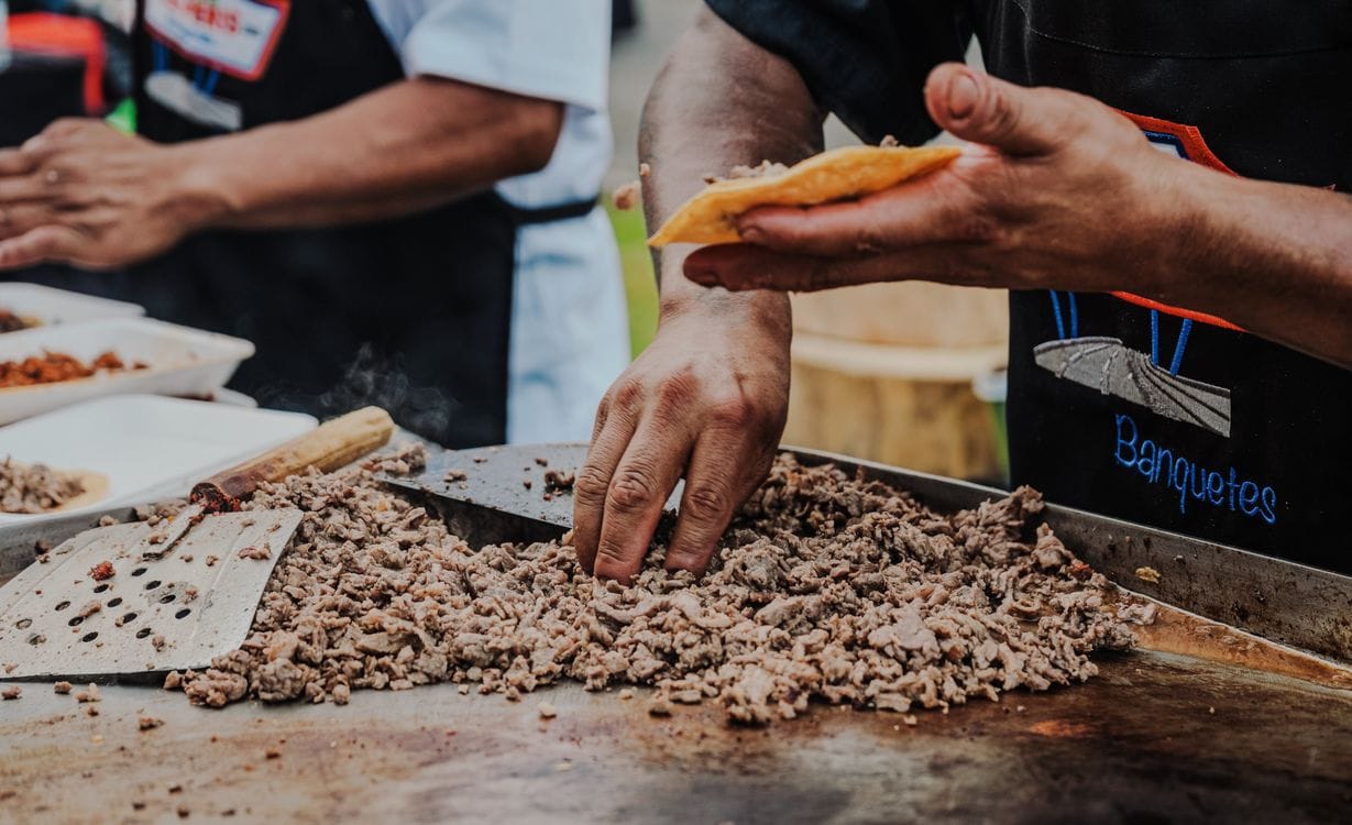 Street food vendor preparing tacos on a hot griddle at an outdoor stall in Mexico