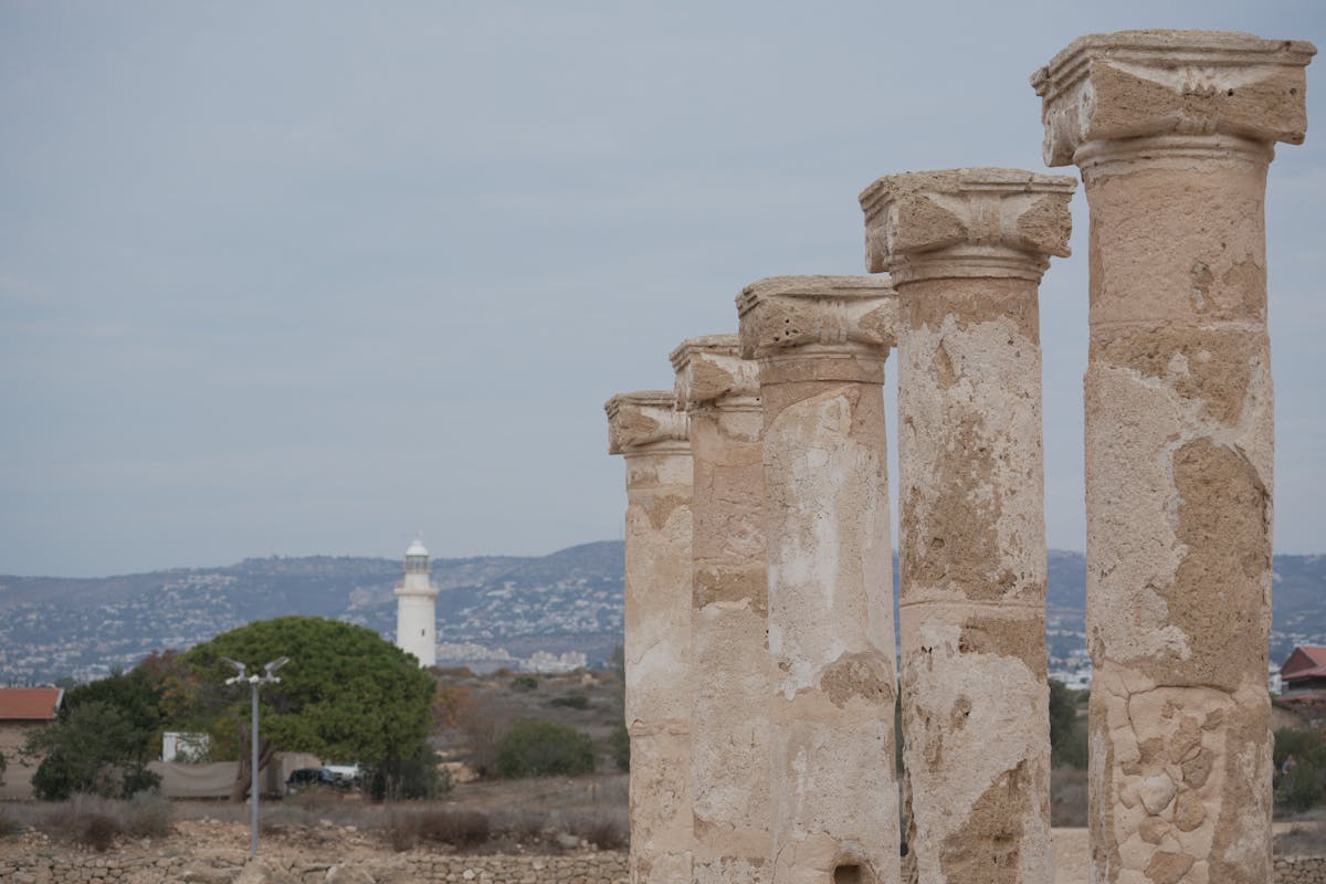 Ancient stone columns at Paphos Archaeological Park with the lighthouse behind