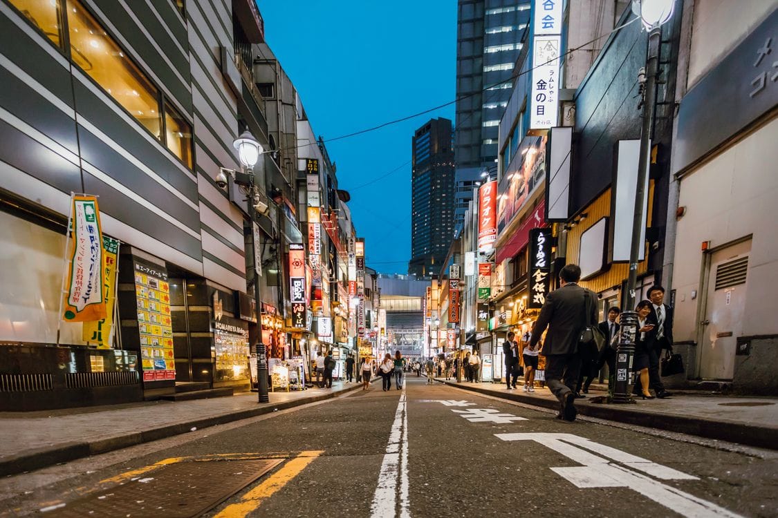 A quiet Tokyo backstreet at dusk, lit by shop signs and lanterns