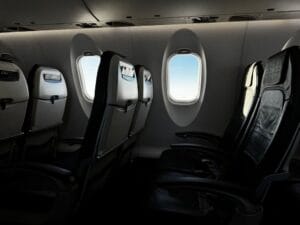 Interior of an empty airplane cabin with rows of seats and blue sky visible through the windows