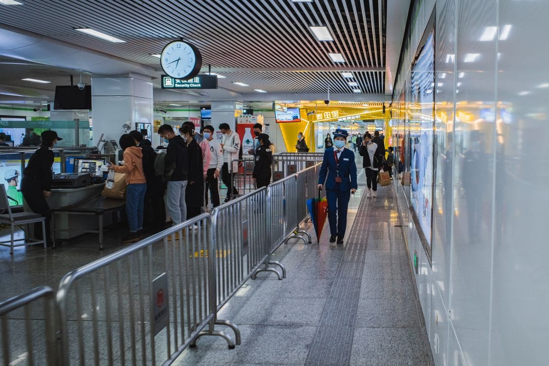 Passengers passing through airport security lane with staff and barriers visible