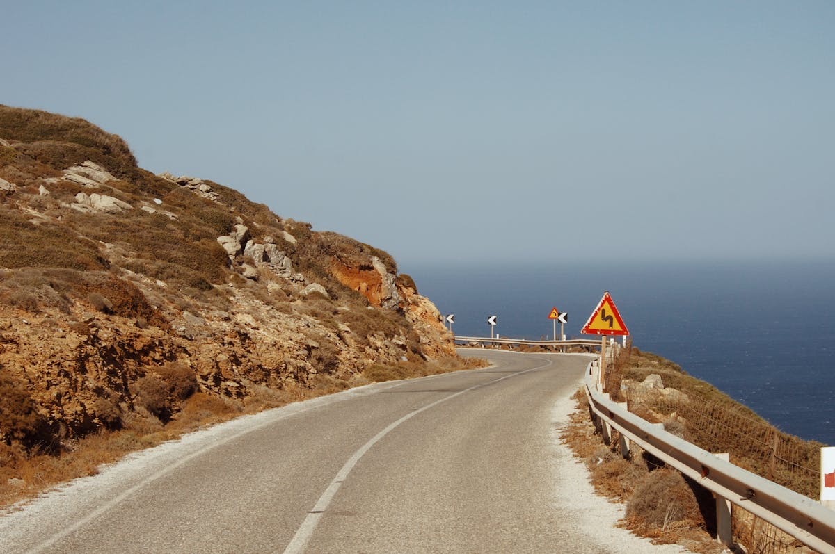 Winding coastal road with a sharp-bend warning sign on a Greek island