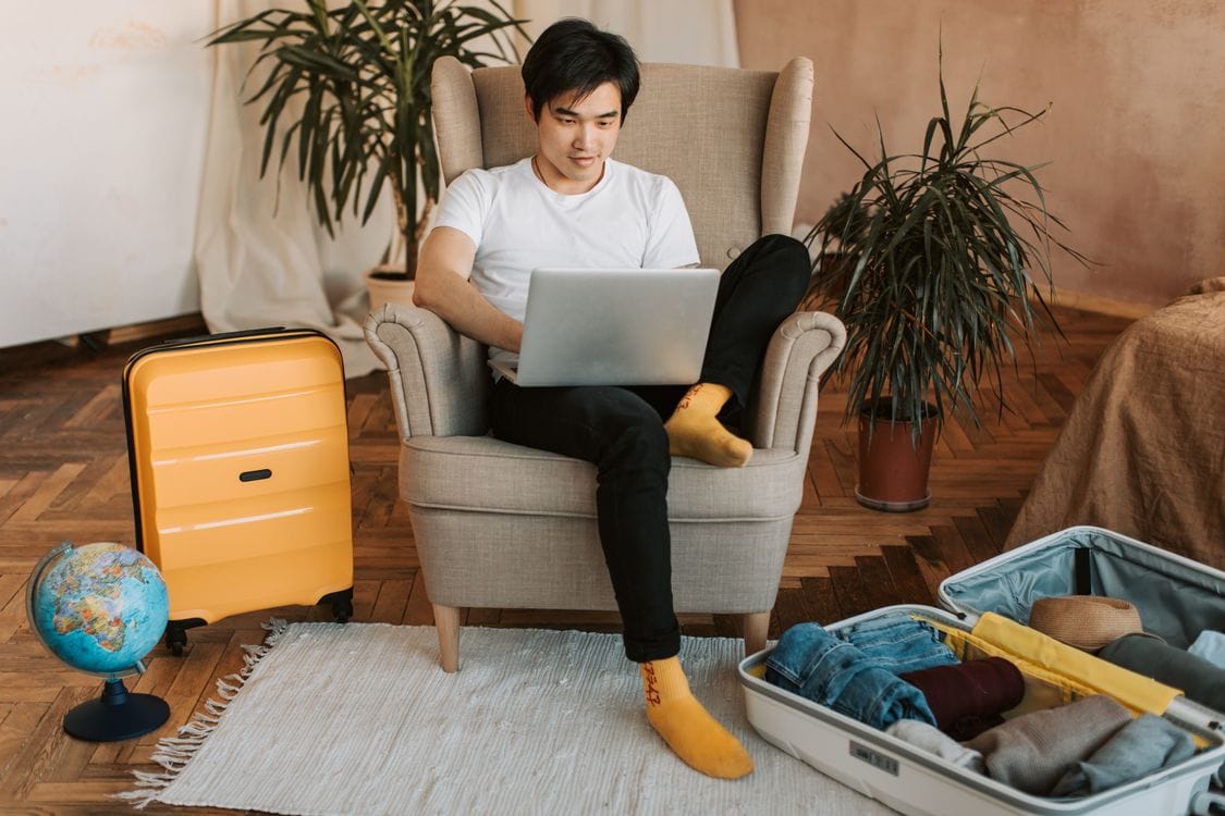 Man planning a holiday on a laptop surrounded by suitcases