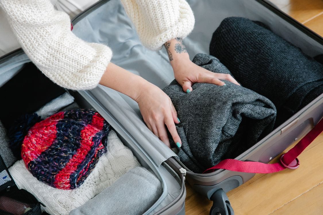 Hands packing clothes into a carry-on suitcase for TUI hand luggage