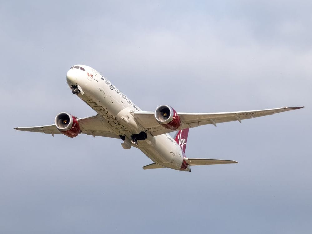 Virgin Atlantic Boeing 787 Dreamliner in flight against a grey overcast sky, red tail fin visible