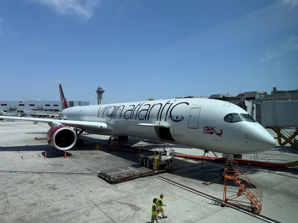 Virgin Atlantic A350 aircraft at an airport gate with clear blue sky and "virgin atlantic" text prominent on the fuselage