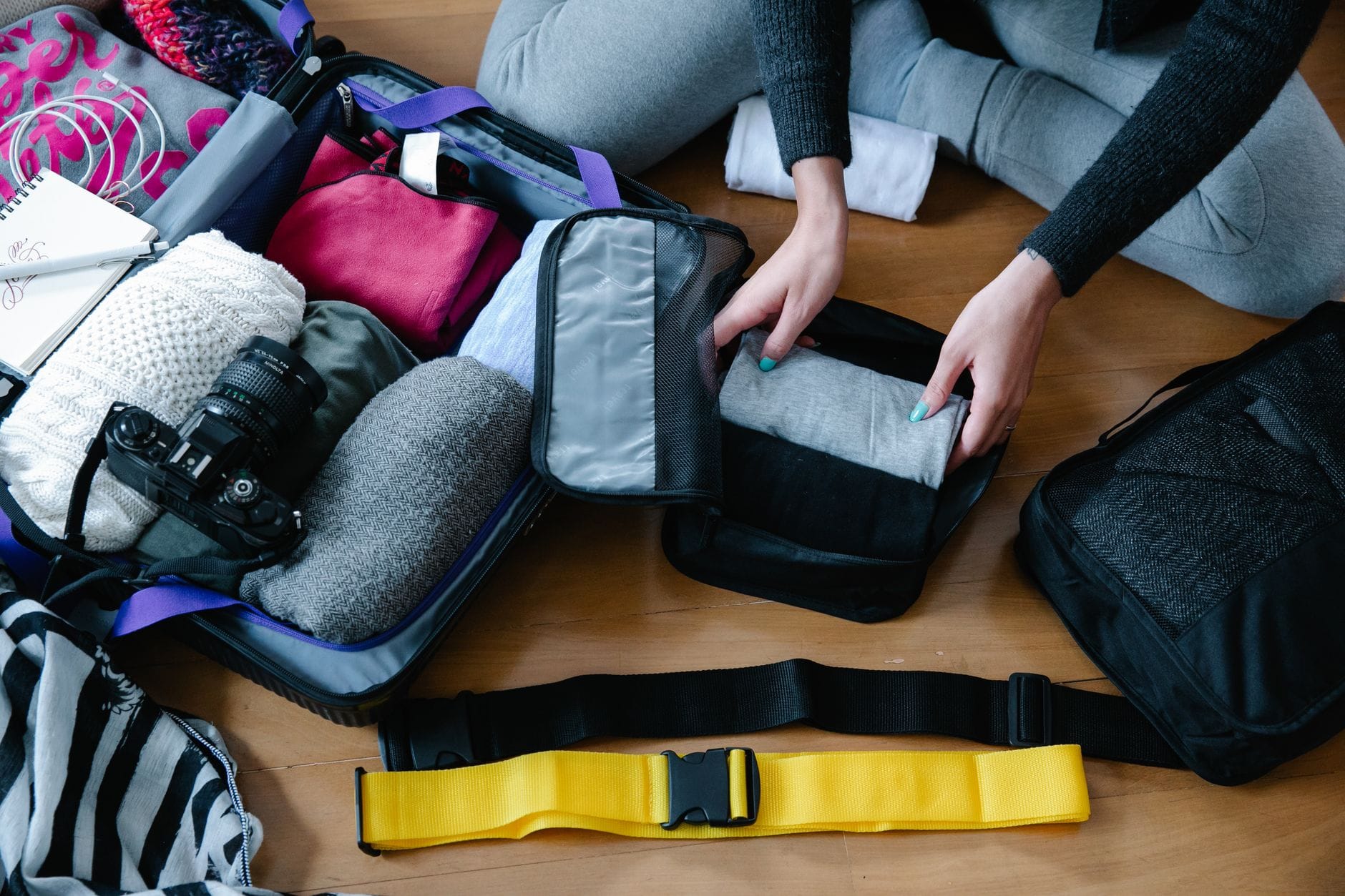 A woman arranging clothes and accessories into a suitcase, preparing for travel