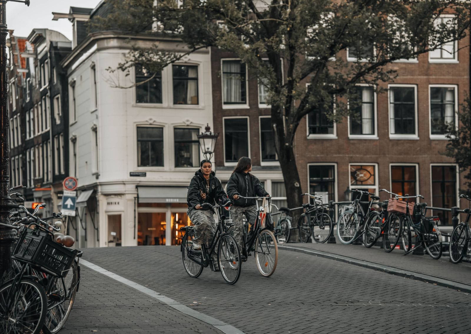 Cyclists crossing a canal bridge lined with parked bikes in Amsterdam