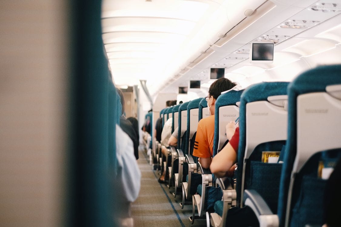 Passengers seated inside an airplane cabin with blue seats, illustrating economy seat rows