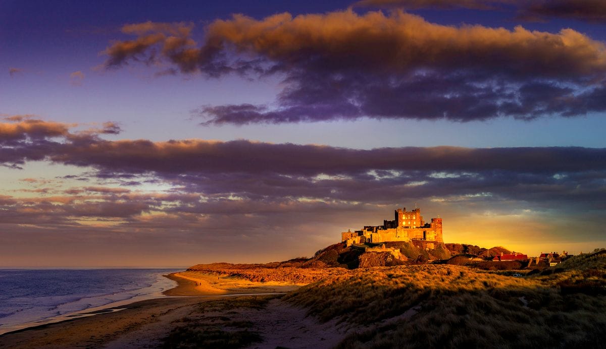 Bamburgh Castle lit gold above the beach at sunset