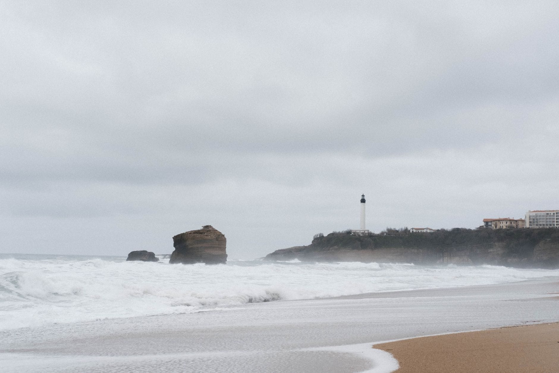 Biarritz's lighthouse and rocky coastline on an overcast day with waves rolling in