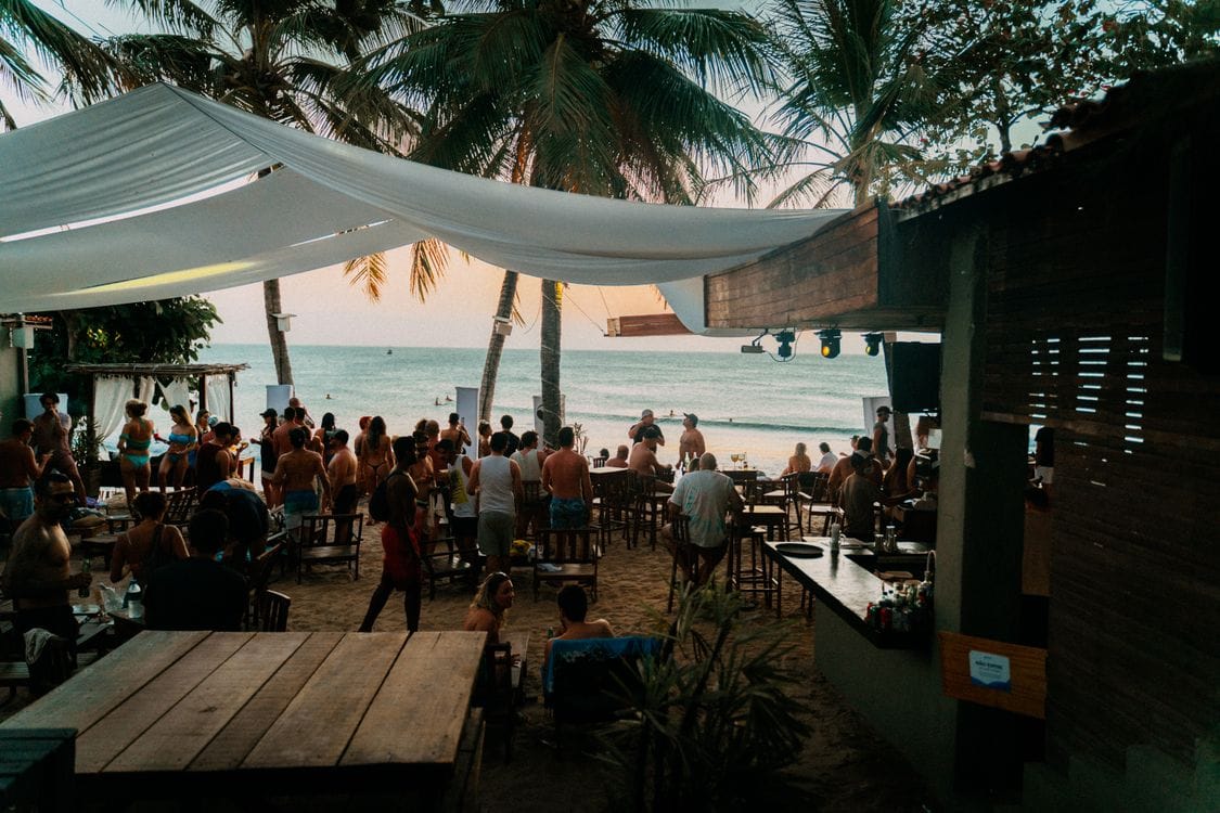 A palm-shaded beach bar filling up with people at sunset