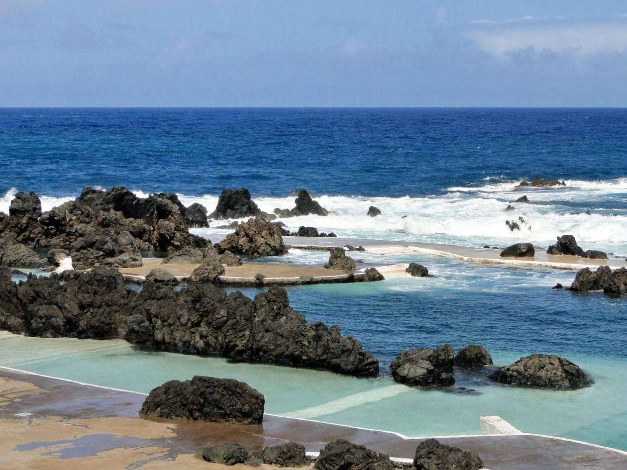 Turquoise water pooling in black volcanic rock beside the ocean