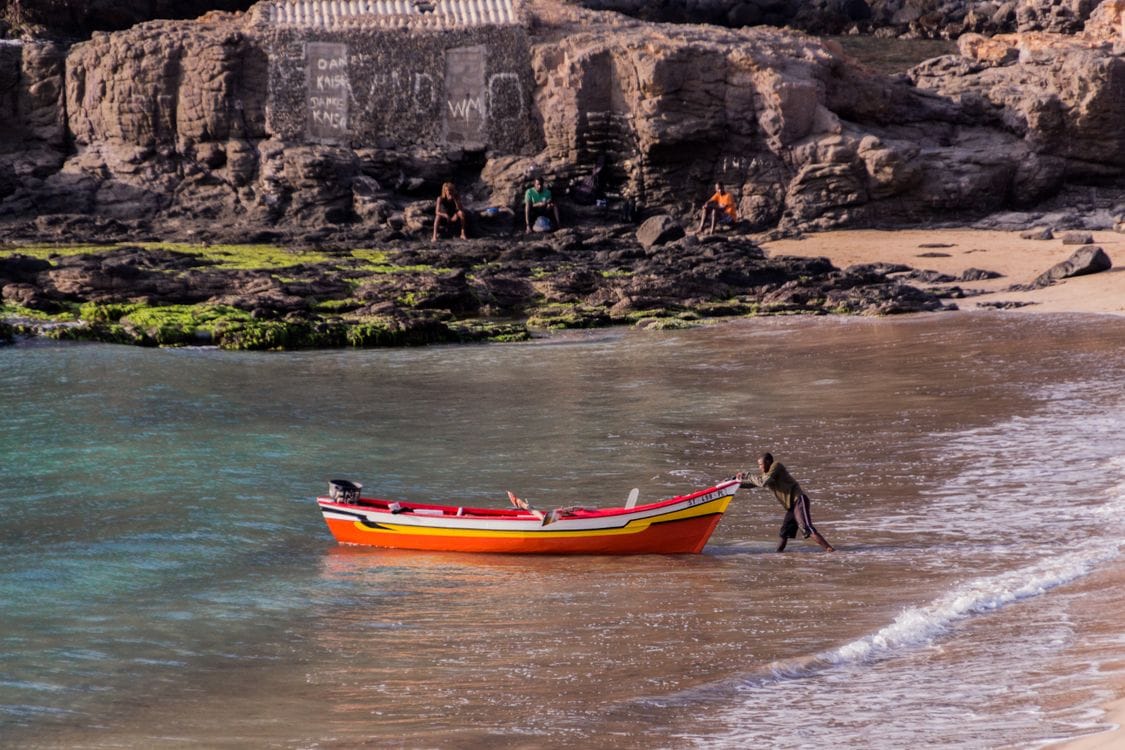 A fisherman pushes a colourful wooden boat onto Tarrafal beach in Cape Verde
