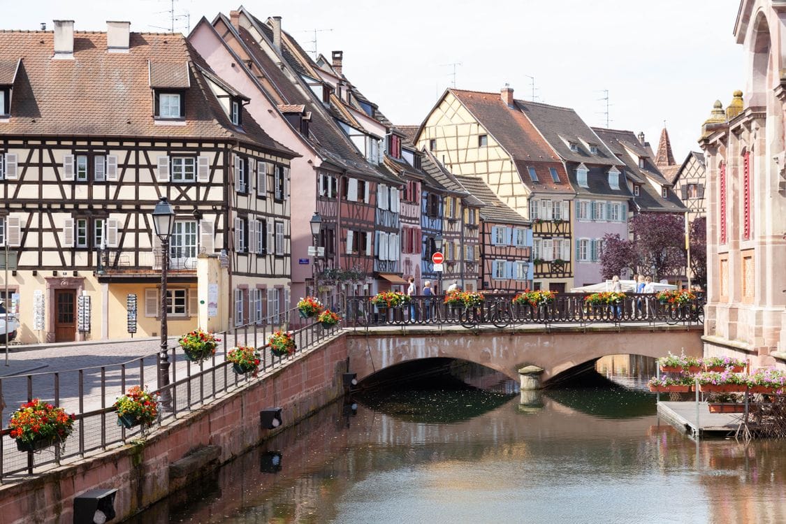 Colourful half-timbered houses along a flower-lined canal bridge in Colmar, Alsace
