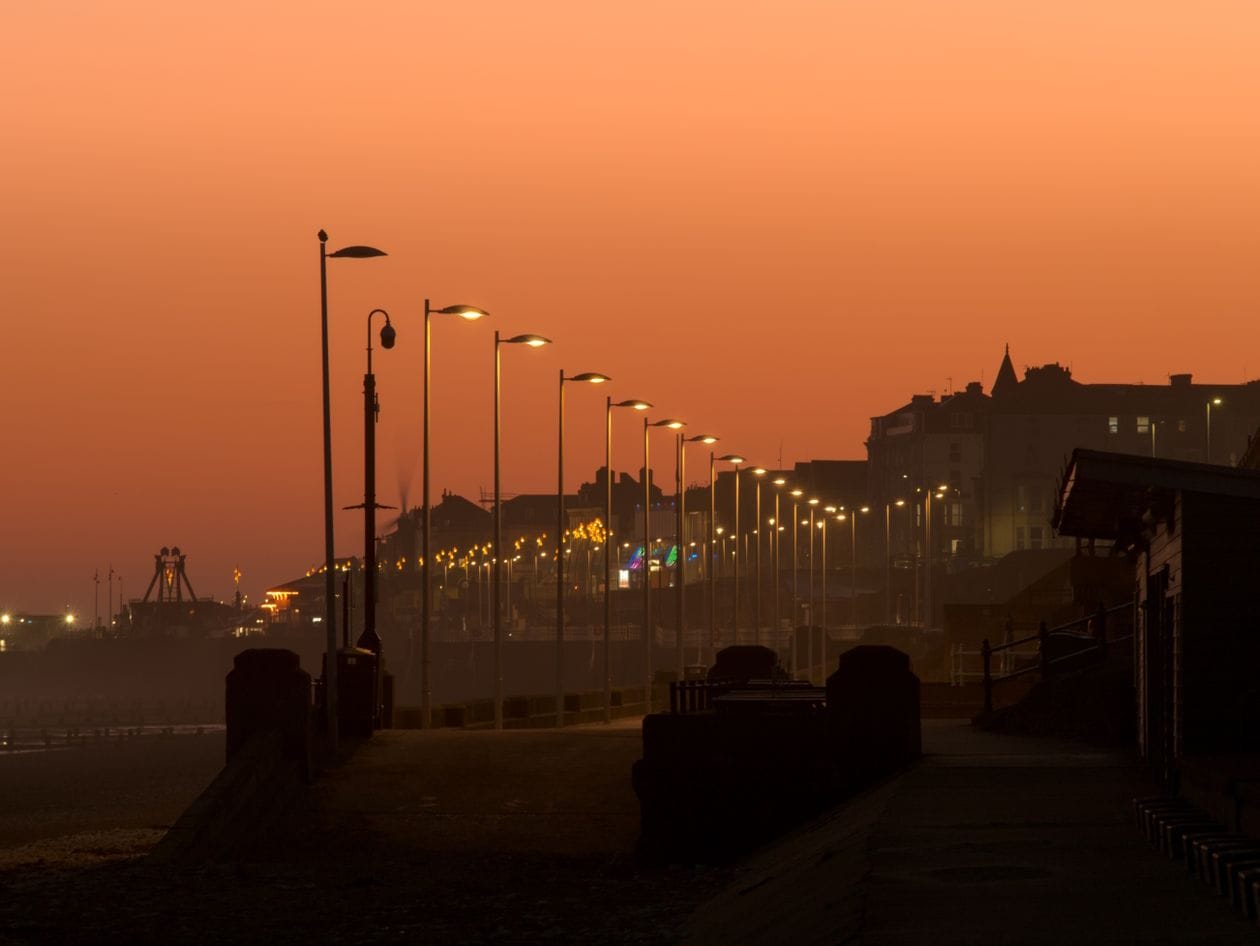 A British seaside promenade lit by streetlamps at dusk