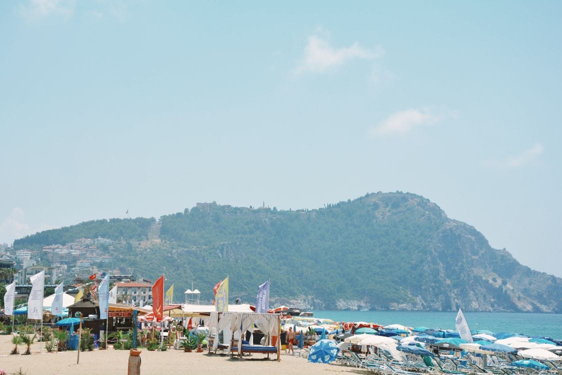Alanya beach in Turkey with sun loungers and a castle hill backdrop, one of On the Beach's Turkish resorts