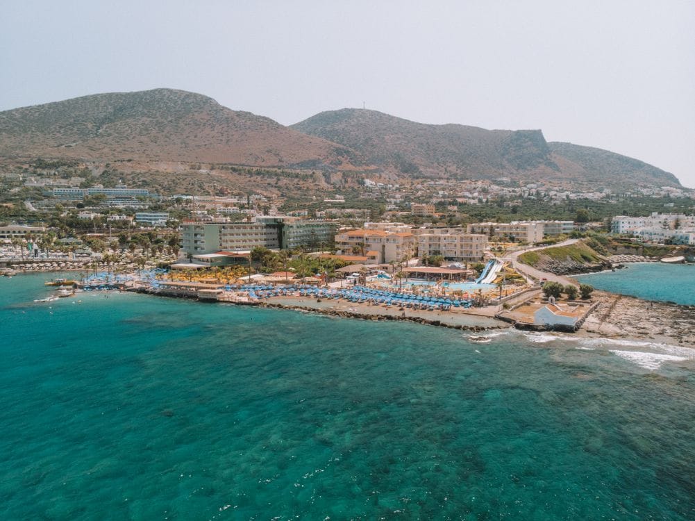 Aerial view of a package holiday resort on the Cretan coast in Greece, with pools, sun loungers and turquoise sea