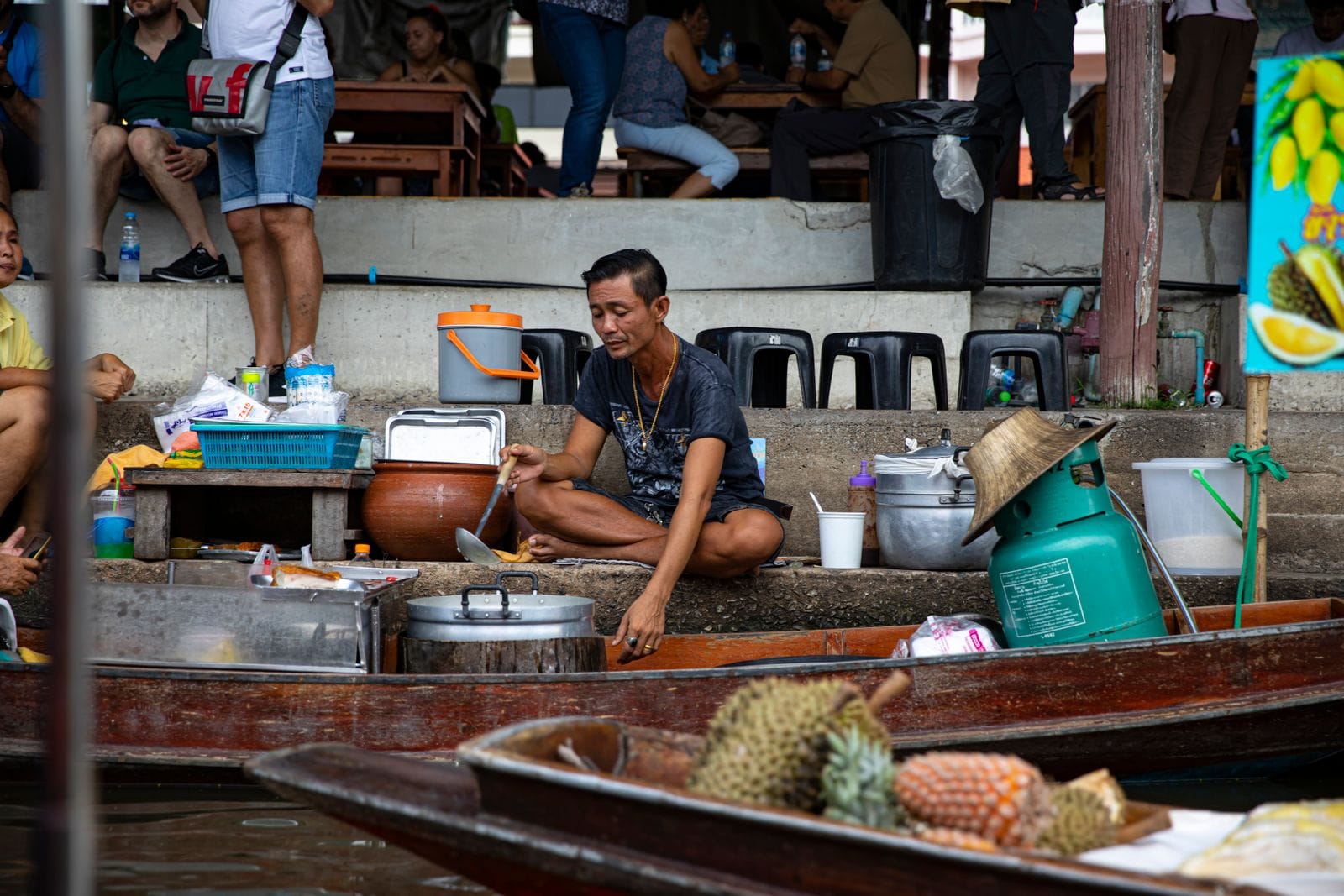 A vendor cooking from a boat at a Thai floating market