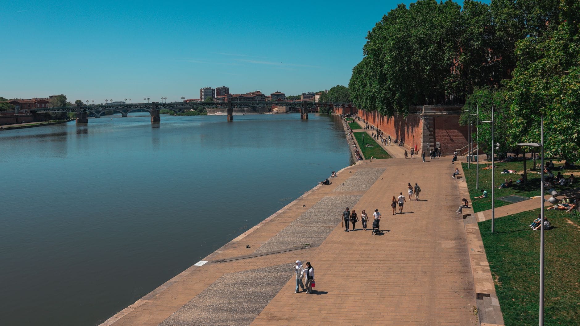 Walkers on the paved quay beside the Garonne river in Toulouse on a clear day
