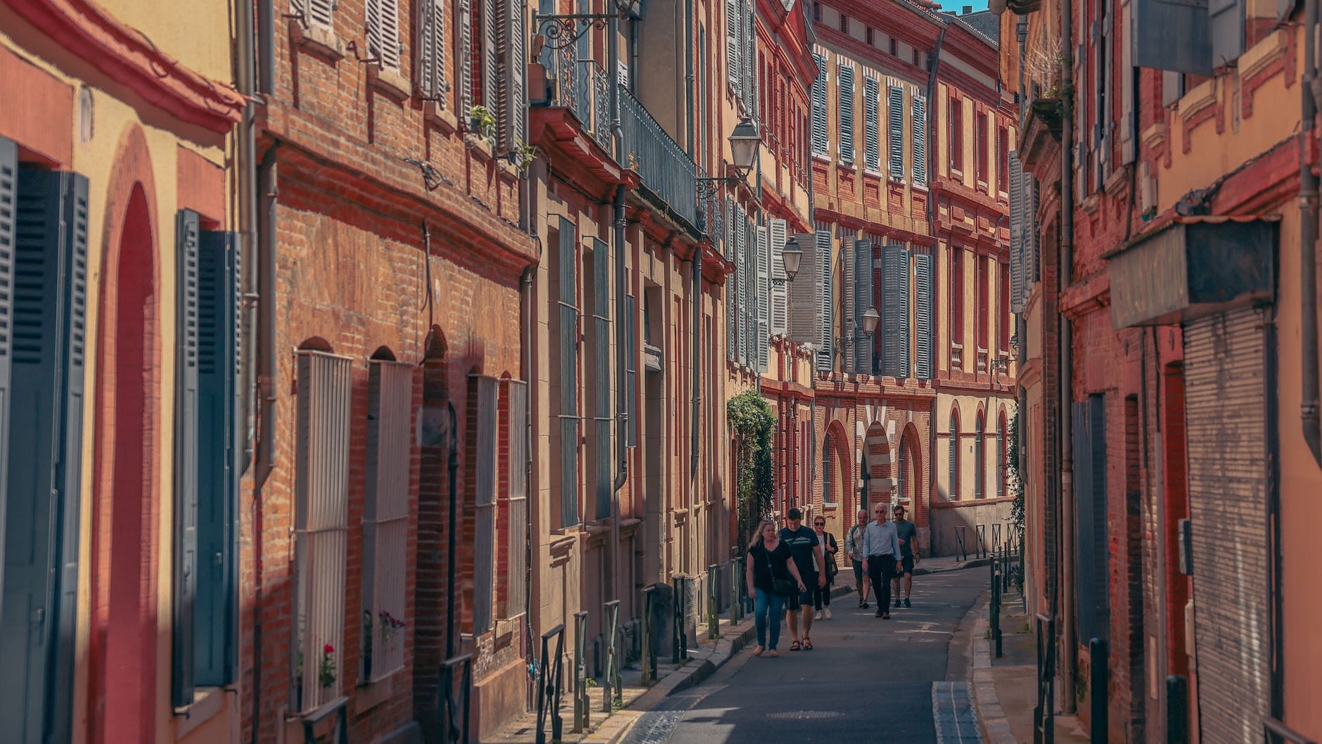 A quiet pink-brick residential street in central Toulouse under a clear sky