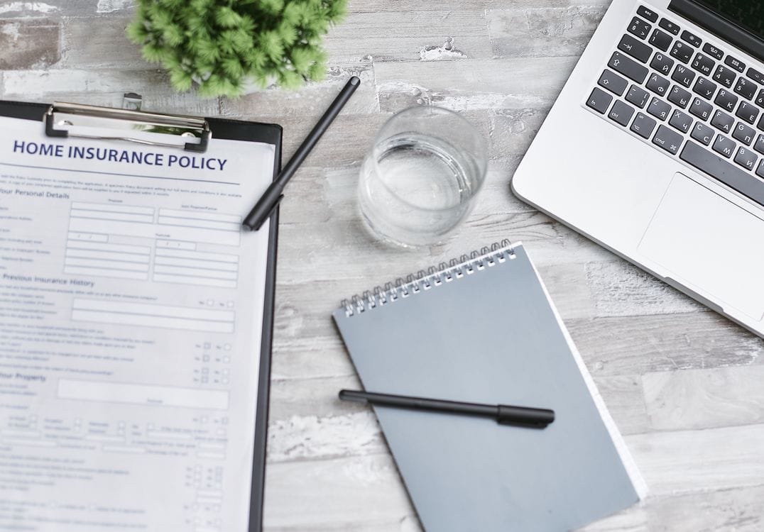 A flatlay of insurance paperwork, a notebook and a laptop on a desk