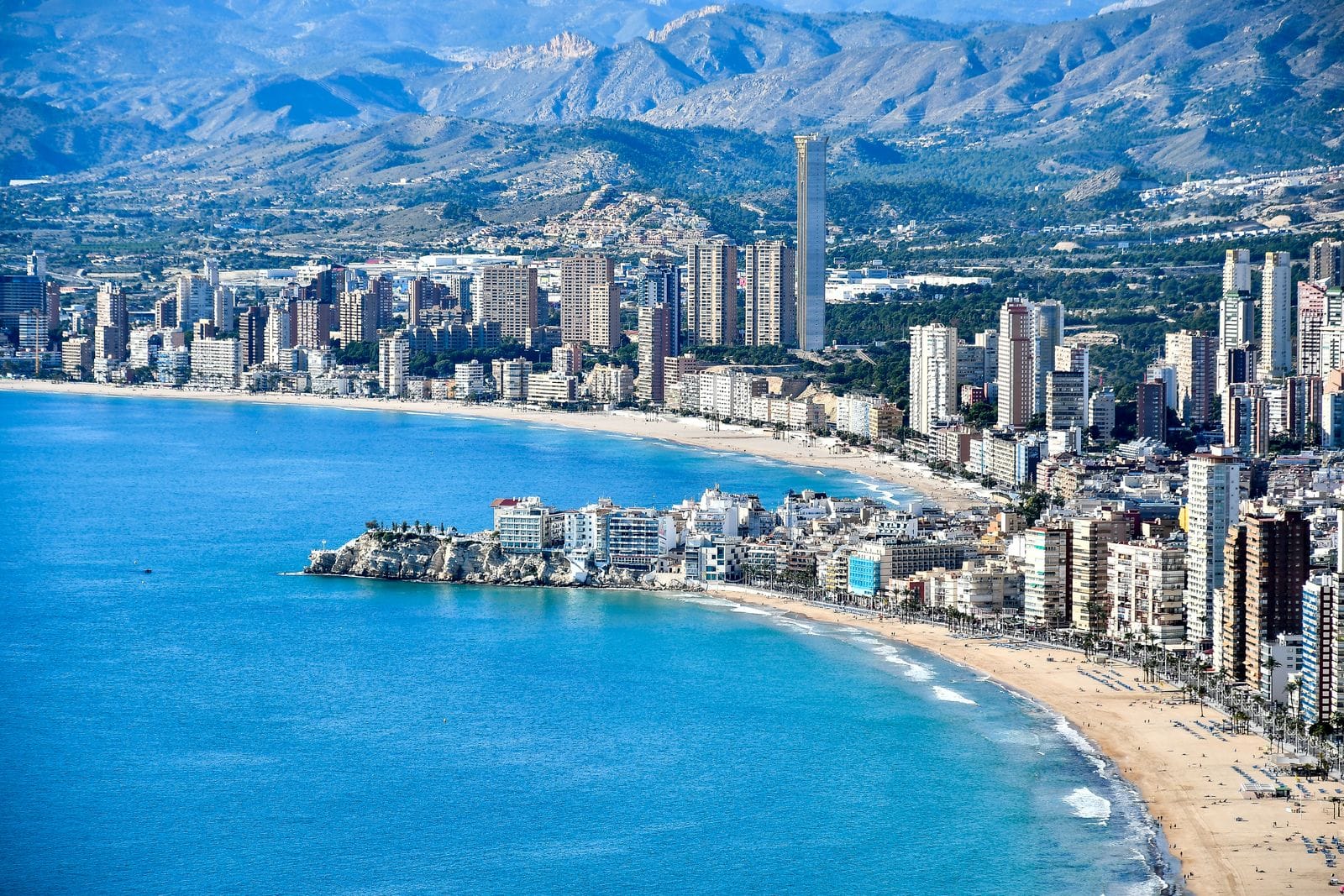 Aerial view of Benidorm's bay, the curve of the beach and the ridge of mountains rising behind the town