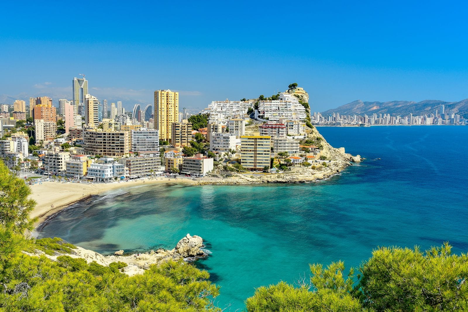 The rocky headland of Benidorm's old town, with pale apartment blocks above a turquoise cove and the modern skyline beyond