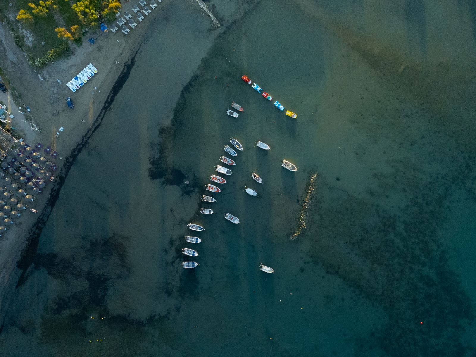 Aerial view of a Corfu beach with rows of sunbeds on the sand and small boats moored in shallow water