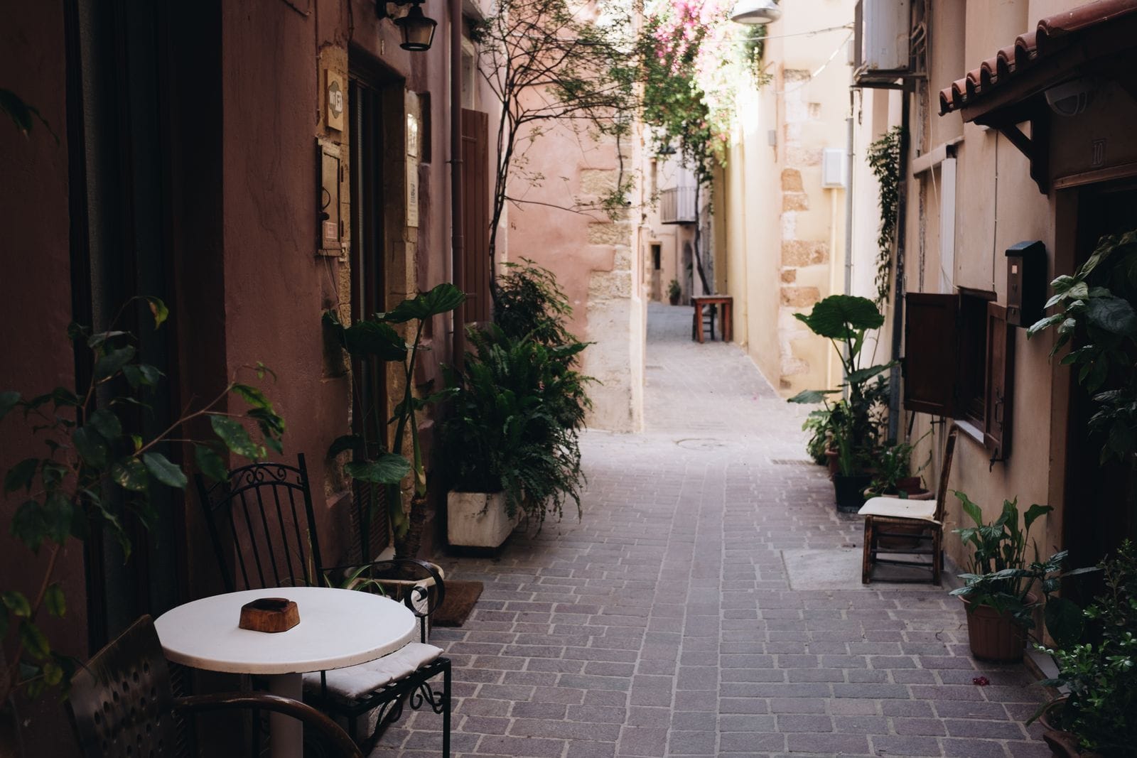 A narrow cobbled lane in Chania Old Town with cafe tables, potted plants and bougainvillea