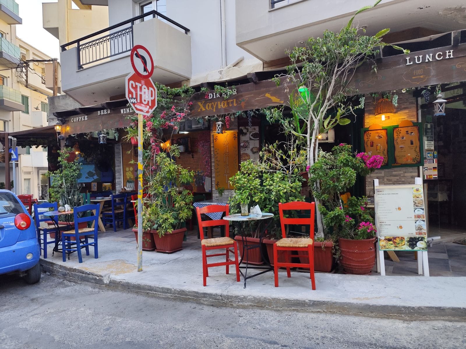 A street-corner taverna in Heraklion with painted chairs, potted plants and a set-menu board outside