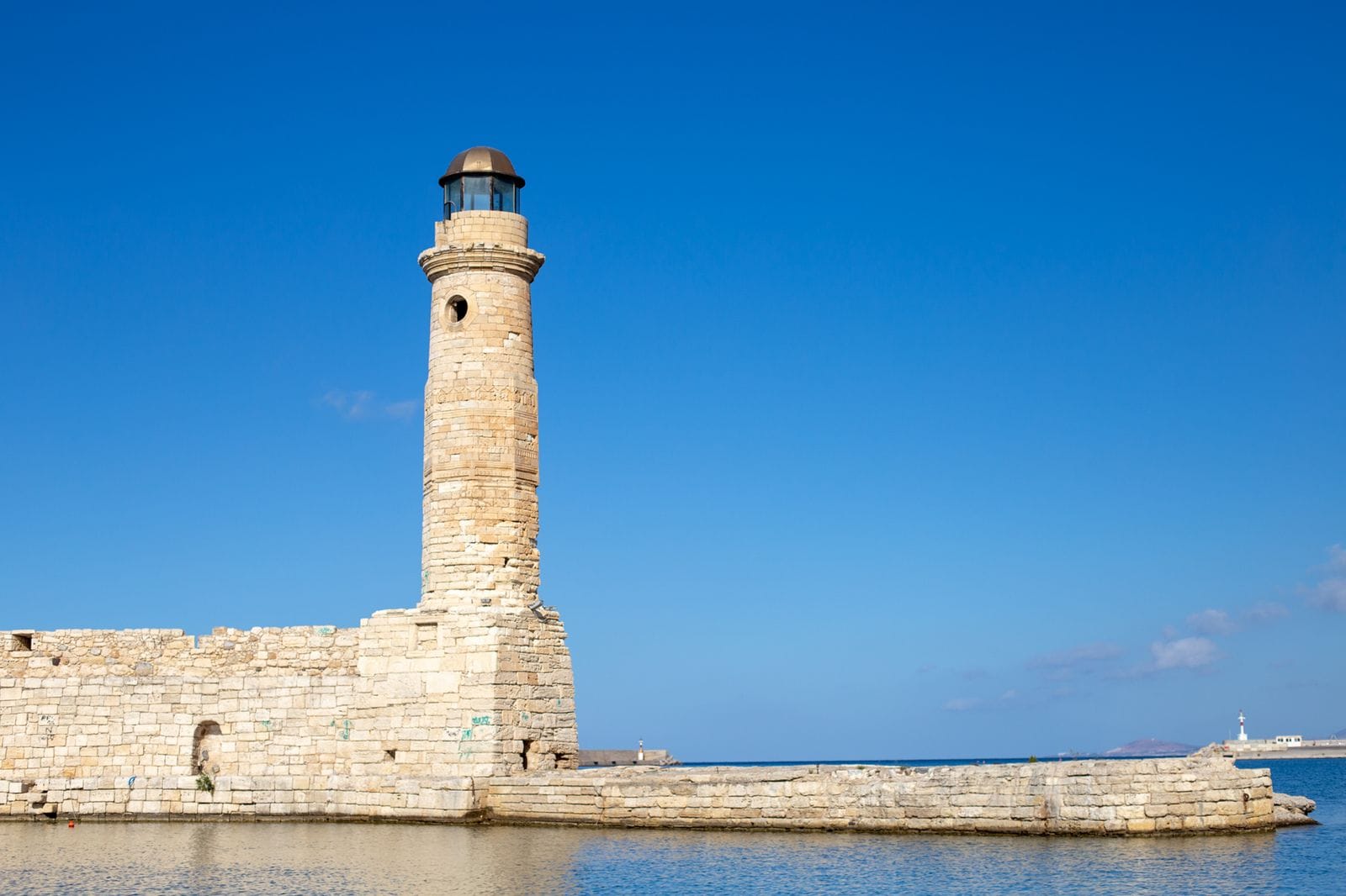 The stone Venetian lighthouse on the harbour wall at Rethymno, Crete, against a deep blue sky