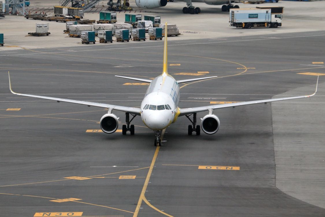A commercial jet taxiing on airport tarmac with ground equipment visible behind
