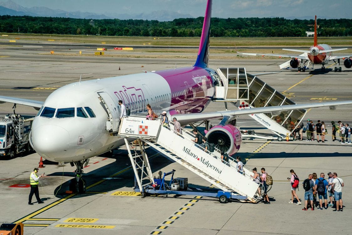 Passengers boarding a Wizz Air aircraft up airstairs at an EU airport, several carrying small bags
