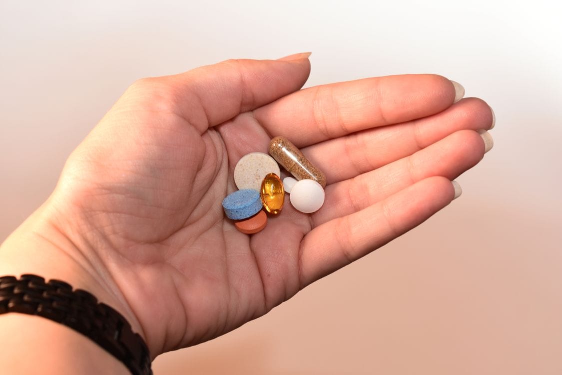 A hand holding a variety of medication pills and capsules