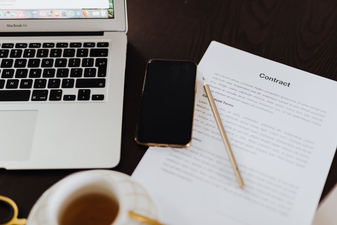A laptop, smartphone and contract document on a desk with a cup of tea