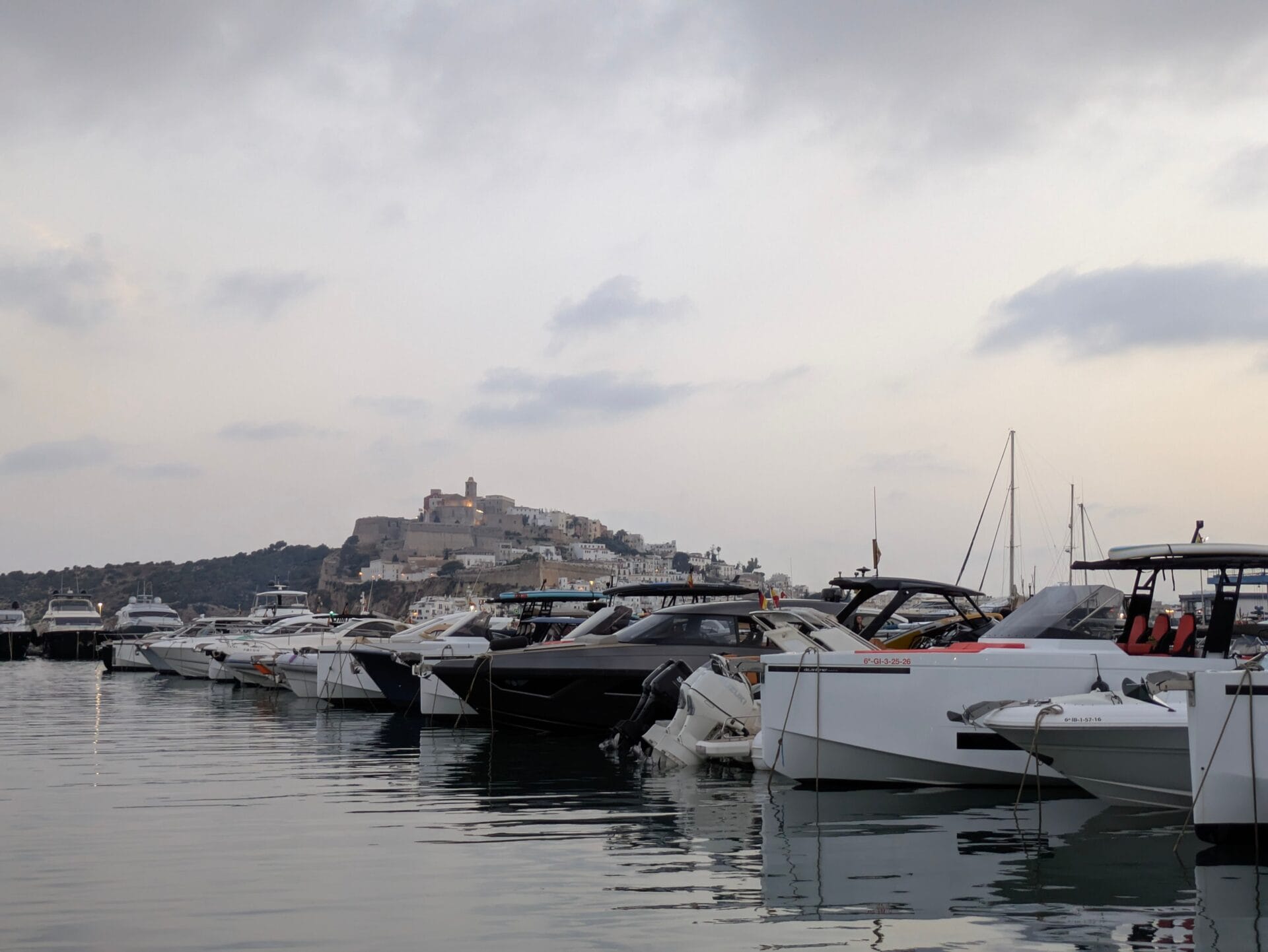 Yachts moored in Ibiza Town's marina at dusk, with Dalt Vila's floodlit cathedral above the harbour