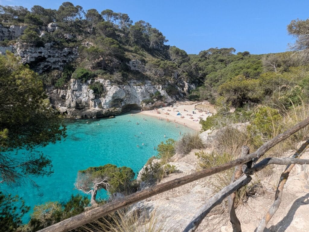 Is Menorca expensive: turquoise water and pine-backed cliffs at Cala Macarella beach near Ciutadella