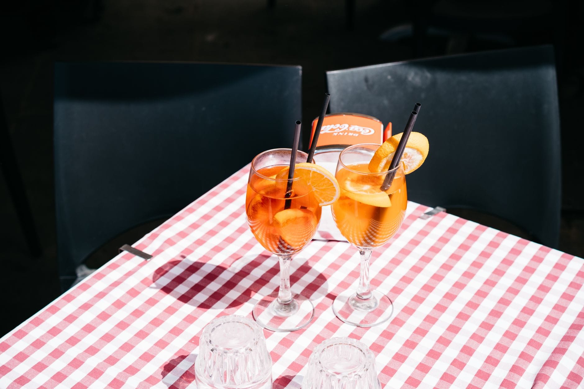 Two Aperol Spritz cocktails on a red and white checked tablecloth, part of a Milan aperitivo