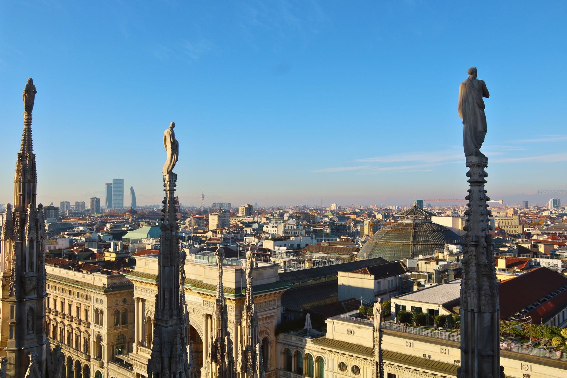 The marble spires and statues of Milan Duomo's rooftop terrace, with the city's modern skyline behind