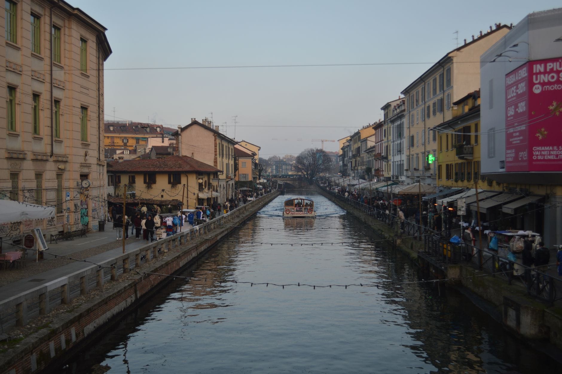 A boat passing along the Naviglio Grande canal in Milan's Navigli district at dusk